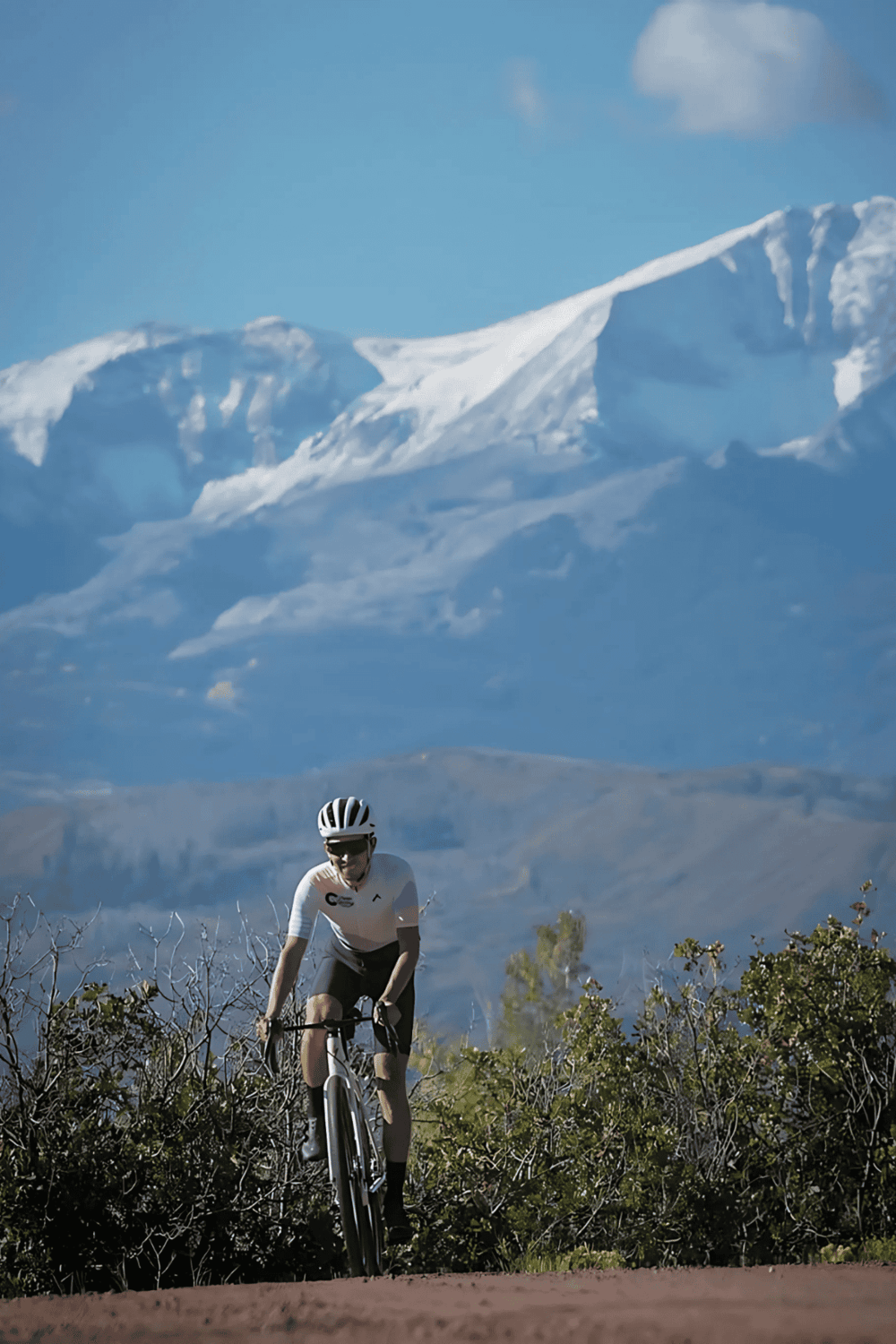 Rugged cyclist riding mountain trail with snowy peaks in background, adventure and outdoor sports.