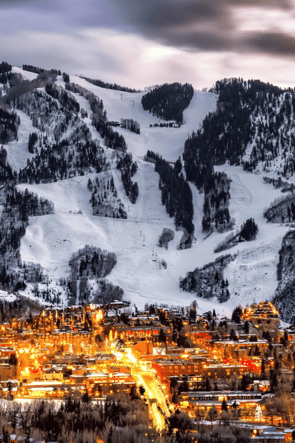 Snowy ski resort mountains with illuminated town below, winter travel destination and mountain adventure.