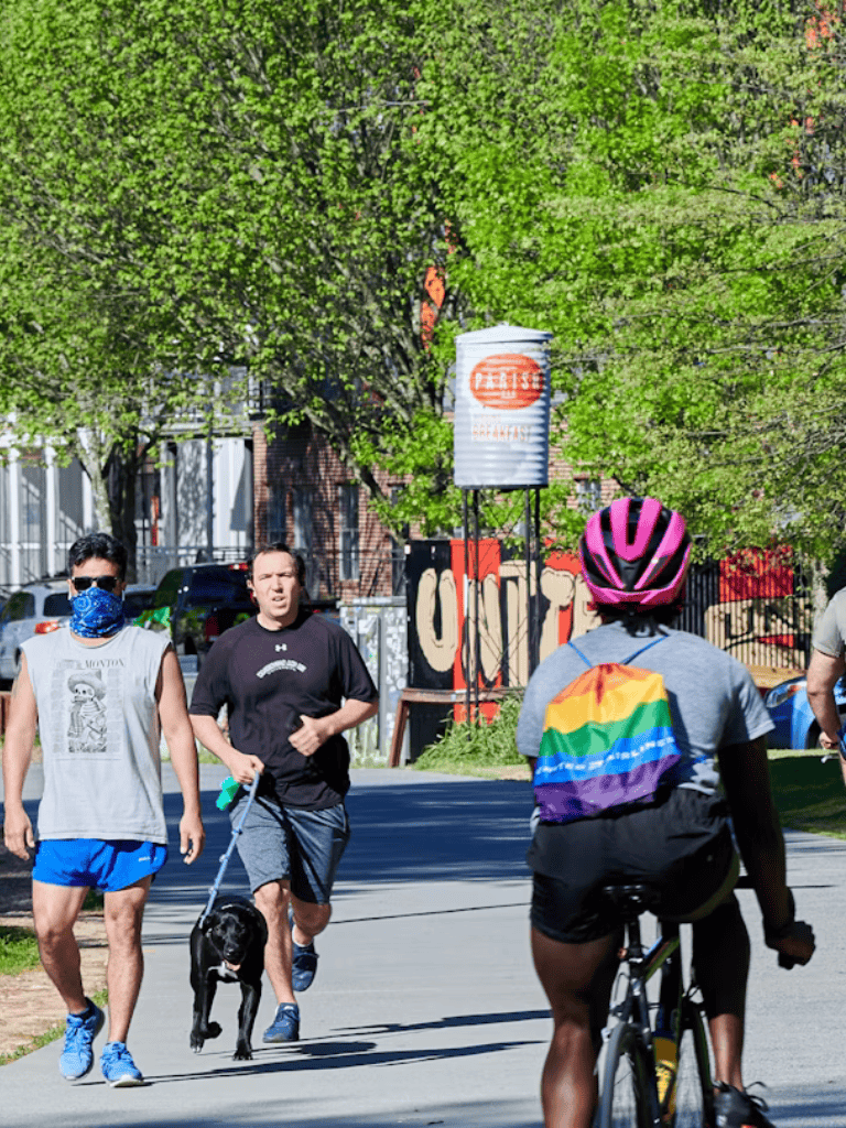 Cute dog walk, joggers and cyclist on city park trail during sunny spring day.