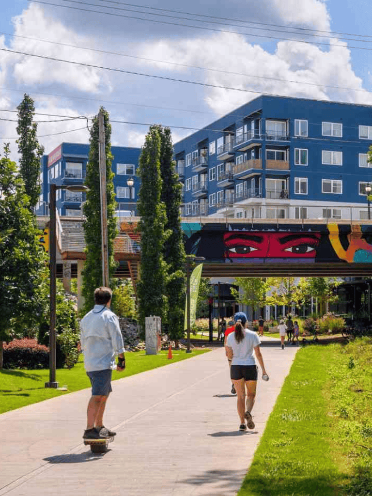 Modern urban outdoor scene with skateboarders, apartment buildings, and vibrant street art in bright daylight.