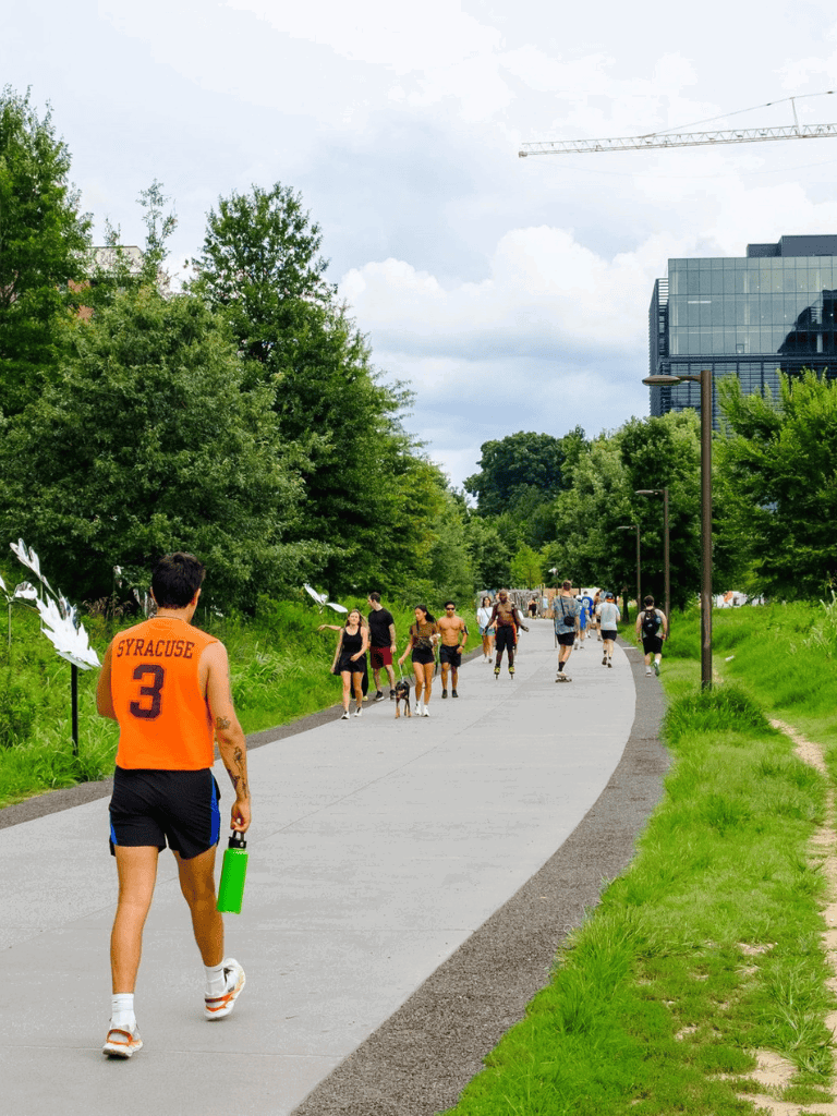 1. People walking and skating on a paved path in a park in front of modern buildings.