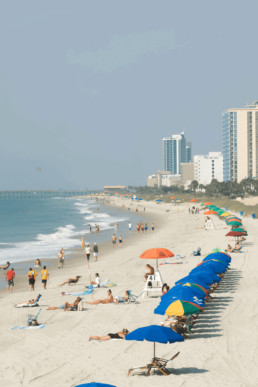 Beach scene with umbrellas, sand, and city skyline, promoting QuestForDirections travel and navigation services.