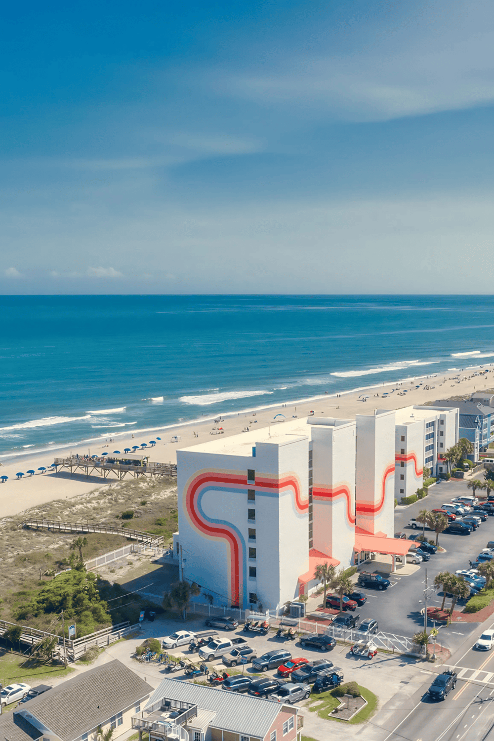 Aerial view of beachfront hotel with ocean waves and blue sky, perfect for vacation and travel planning.