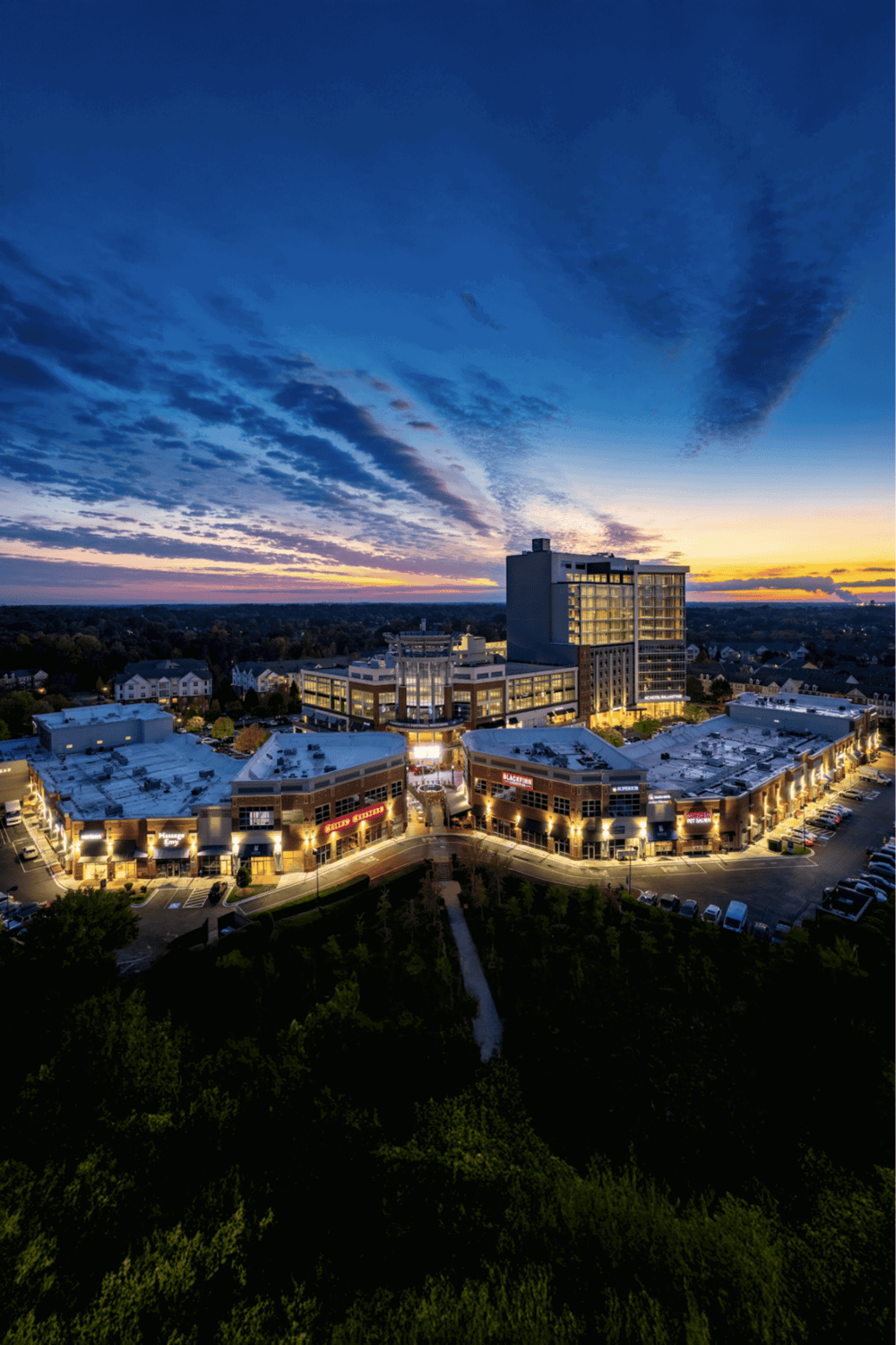 Modern shopping center with retail stores and entertainment, sunset sky, urban commercial complex.