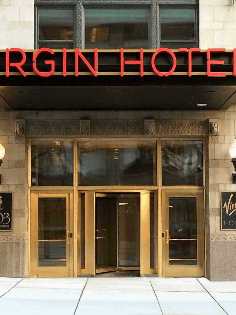 Modern hotel entrance with gold door frames and "Virgin" hotel signage.