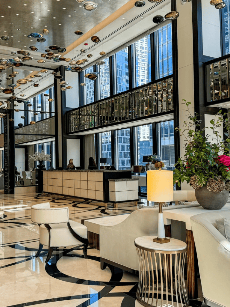 Stylish hotel lobby with modern decor, high ceilings, and large windows showcasing a cityscape.