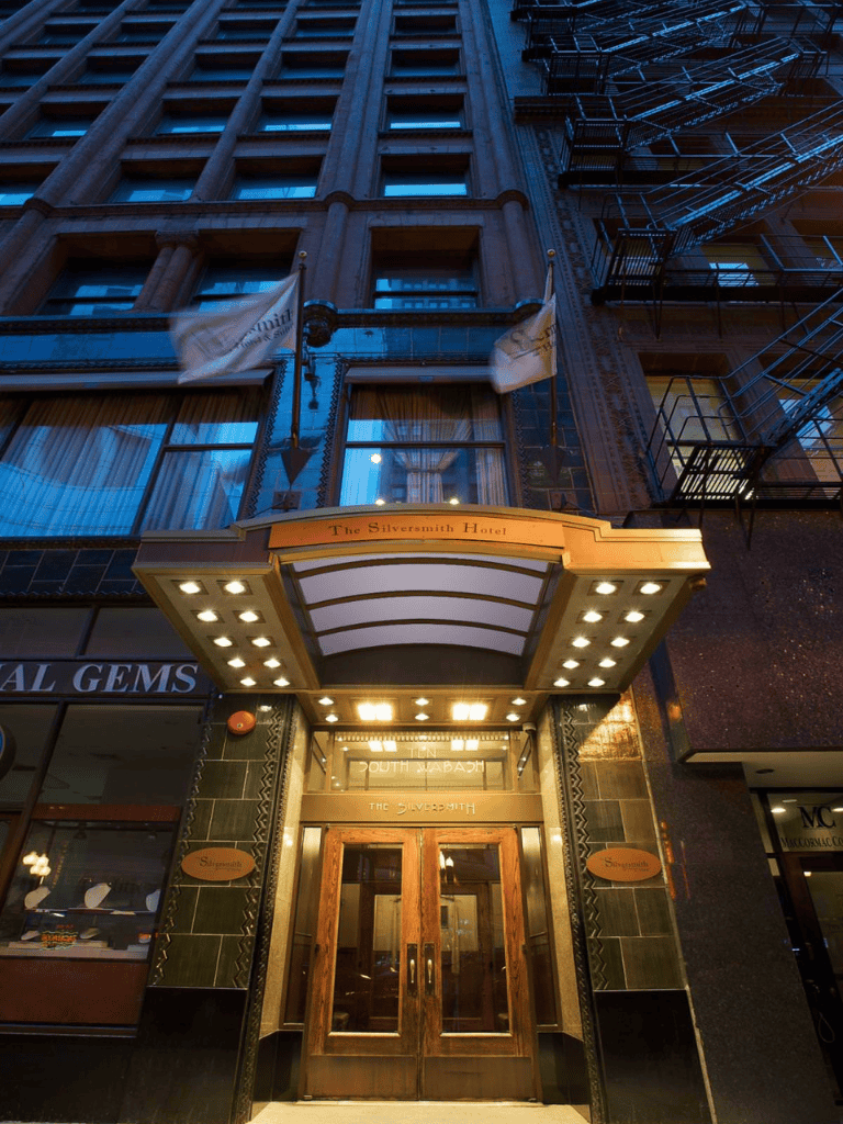 Vintage hotel entrance with illuminated canopy and fire escape on an urban street.