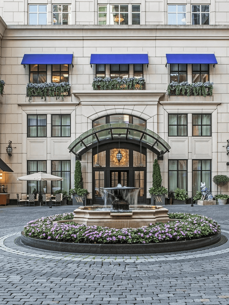 Charming hotel entrance with fountain, outdoor seating, and vibrant floral landscaping.