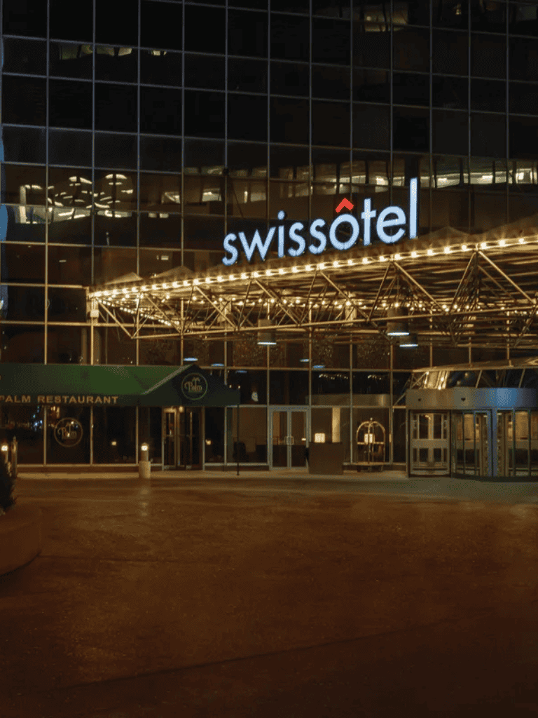 Modern Swissotel hotel exterior at night with illuminated sign and glass facade.