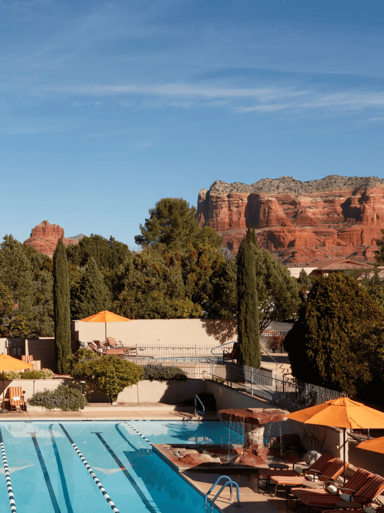 Relaxing outdoor pool area surrounded by desert landscape with red rocks and lush greenery.