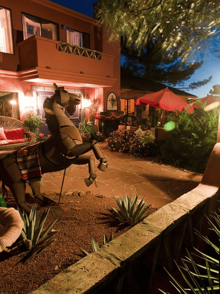 Colorful outdoor patio with a decorative horse sculpture, lush plants, and cozy seating under warm lighting at dusk.