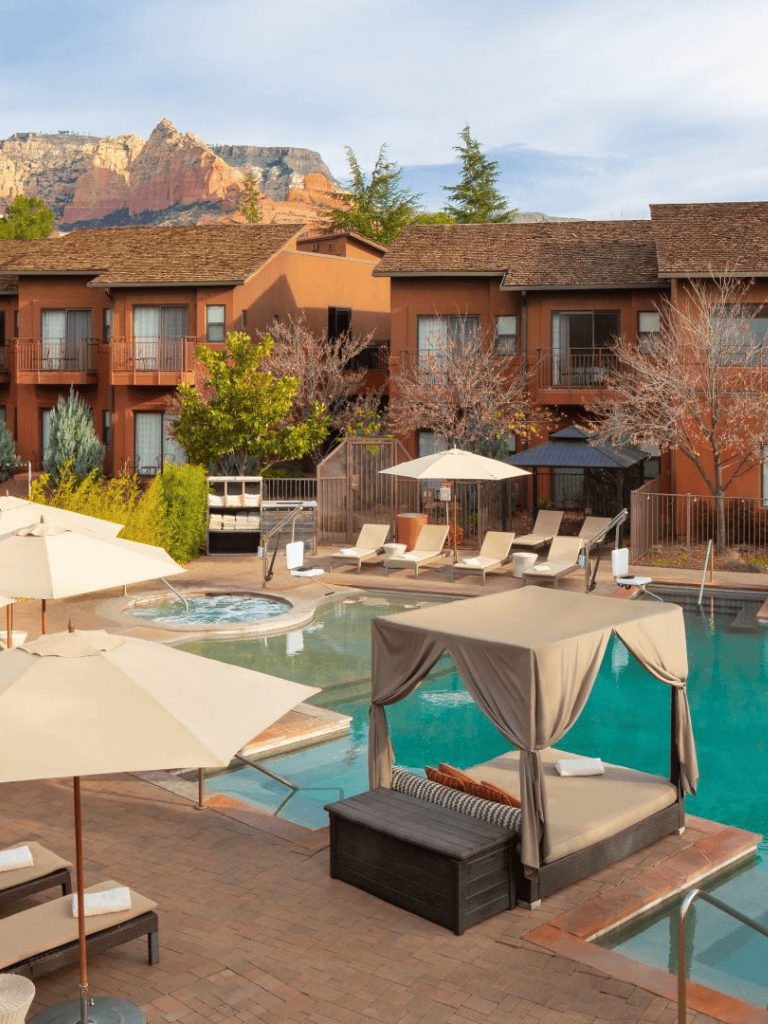 Relaxing hotel pool with lounge chairs and cabanas near red-brick motel buildings and scenic mountains.