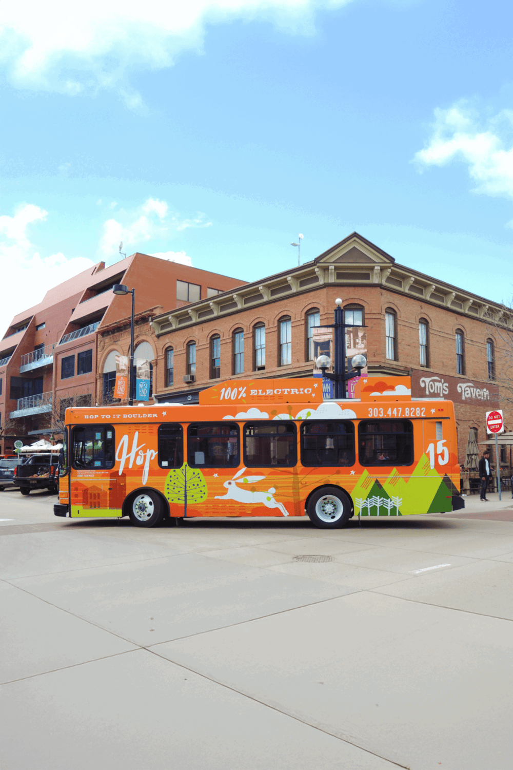 Bright electric trolley bus in downtown with colorful cityscape and historic buildings in background, Denver transportation.