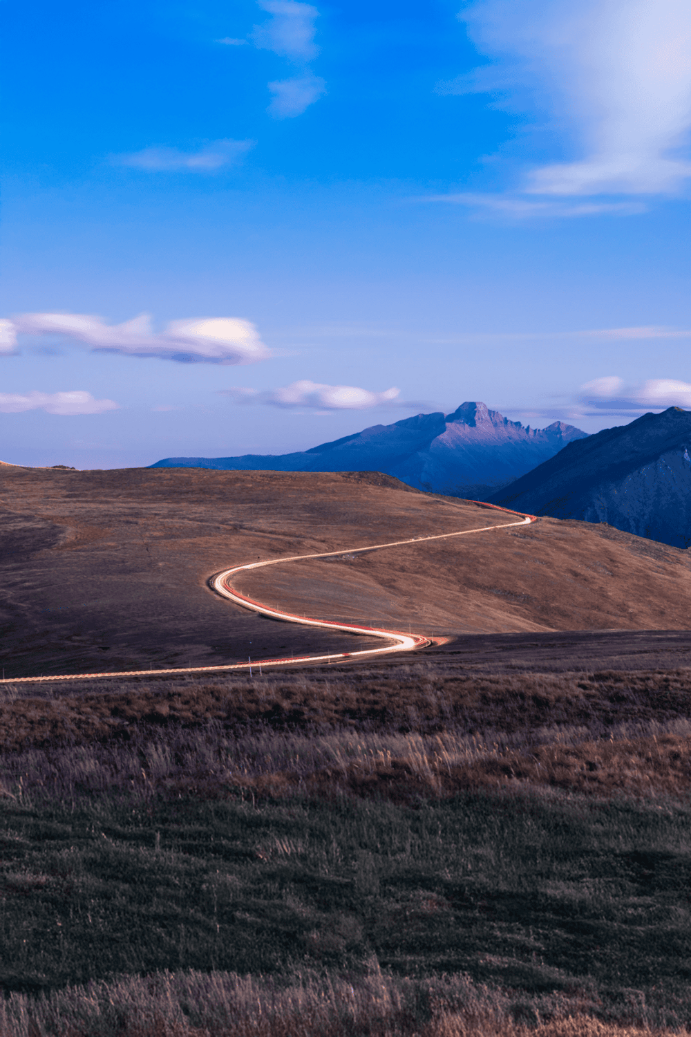 Winding mountain road with scenic landscape and blue sky, ideal for travel and adventure seekers.