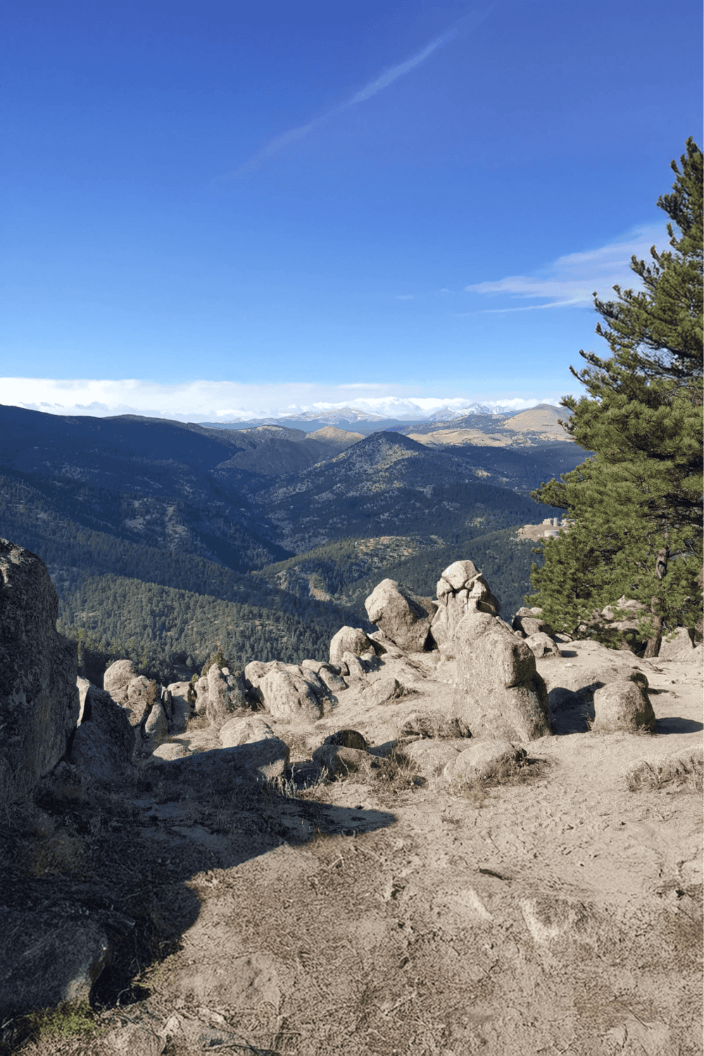 Cliffside mountain view with rocks, trees, and distant snow-capped peaks, perfect for adventure and outdoor exploration.