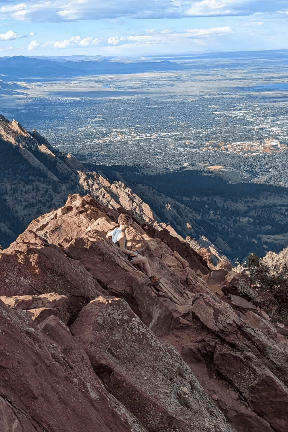 Aerial view of a woman resting on rocky mountain ridge overlooking a cityscape and distant plains.