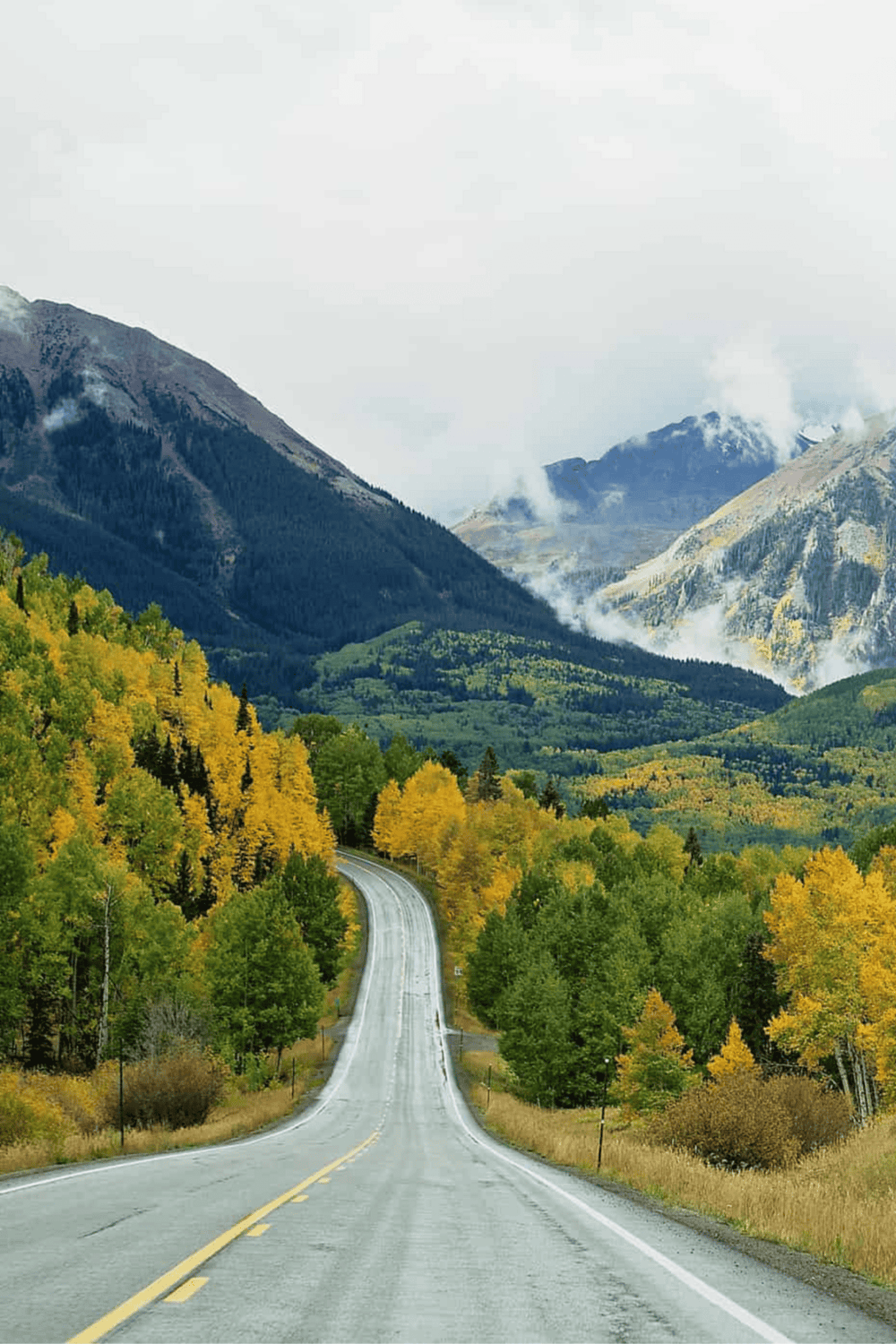 Open road through forested mountains in fall with scenic mountain views, traveling for adventure and exploration.