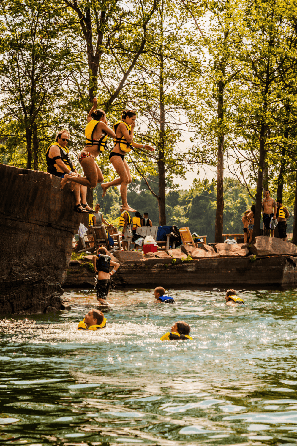 Popular outdoor water activities, families swimming near rocky shoreline, lush green trees.