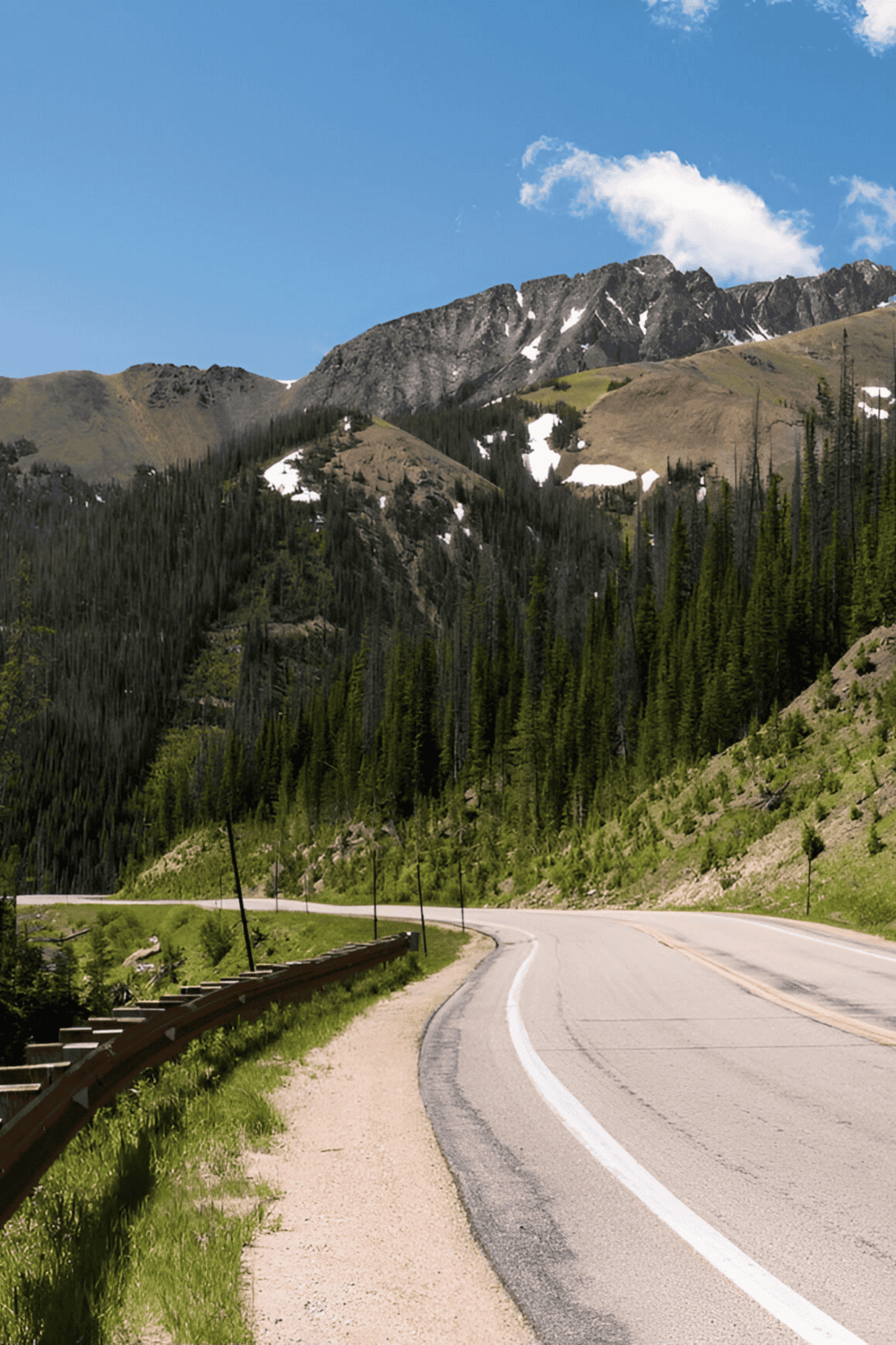 Scenic mountain road with lush forest and clear blue sky, perfect for travel navigation and outdoor adventures.