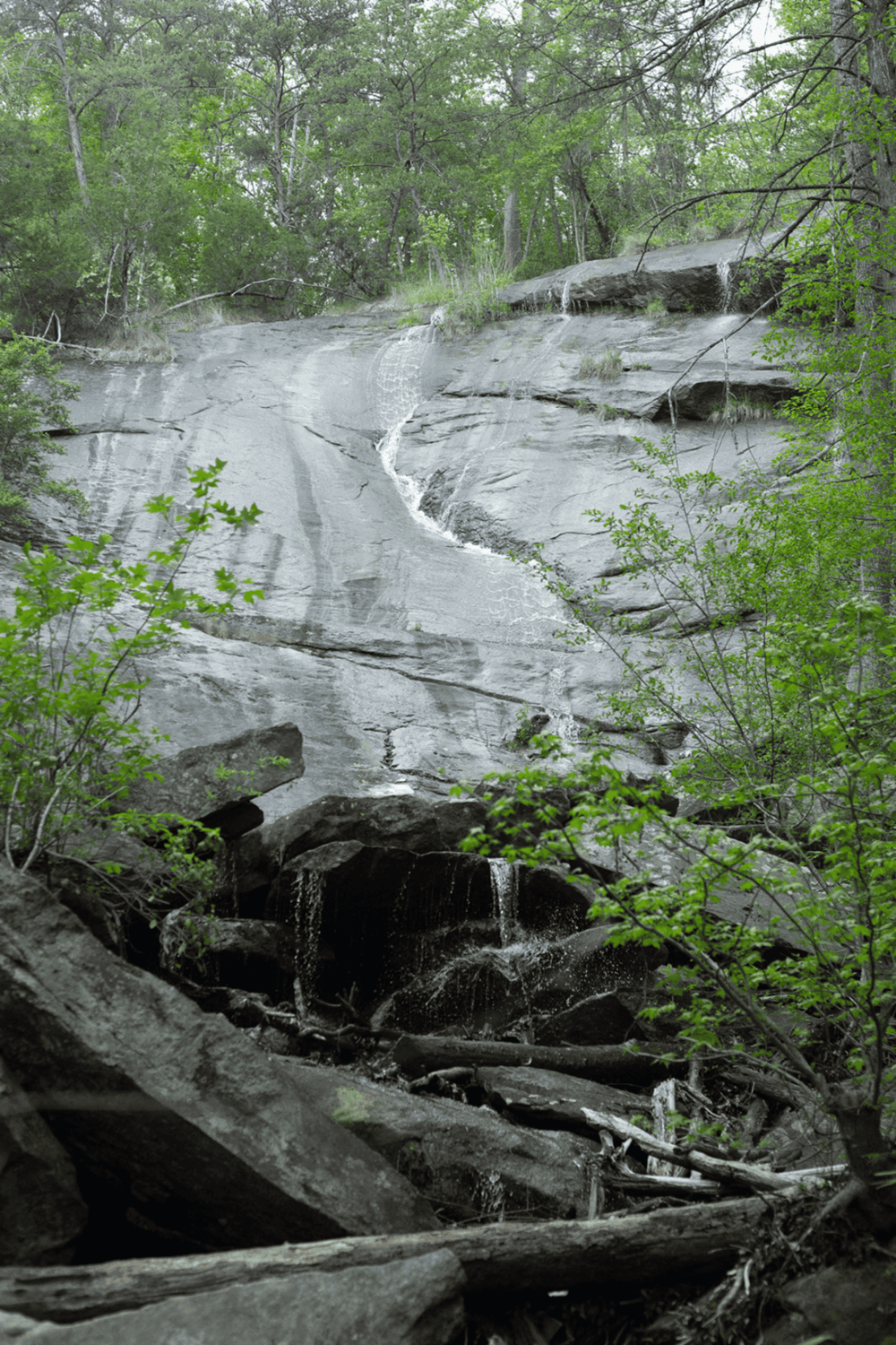 Flowing waterfall in lush forest with rocks and greenery, scenic outdoor nature trail.