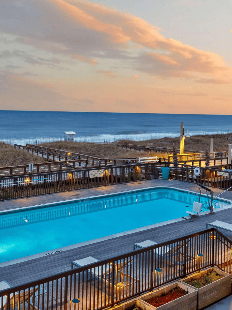 Relaxing ocean view poolside at sunset with boardwalk and beach in the background.