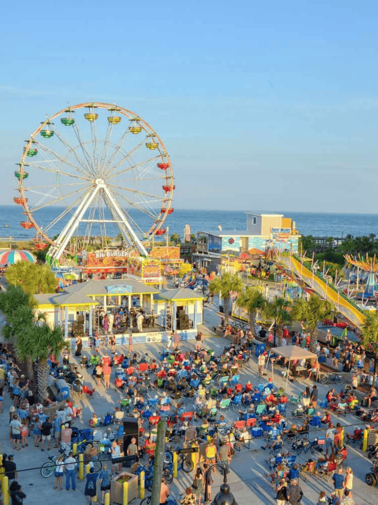 Colorful amusement park at the beach with a ferris wheel and crowds enjoying the attractions.