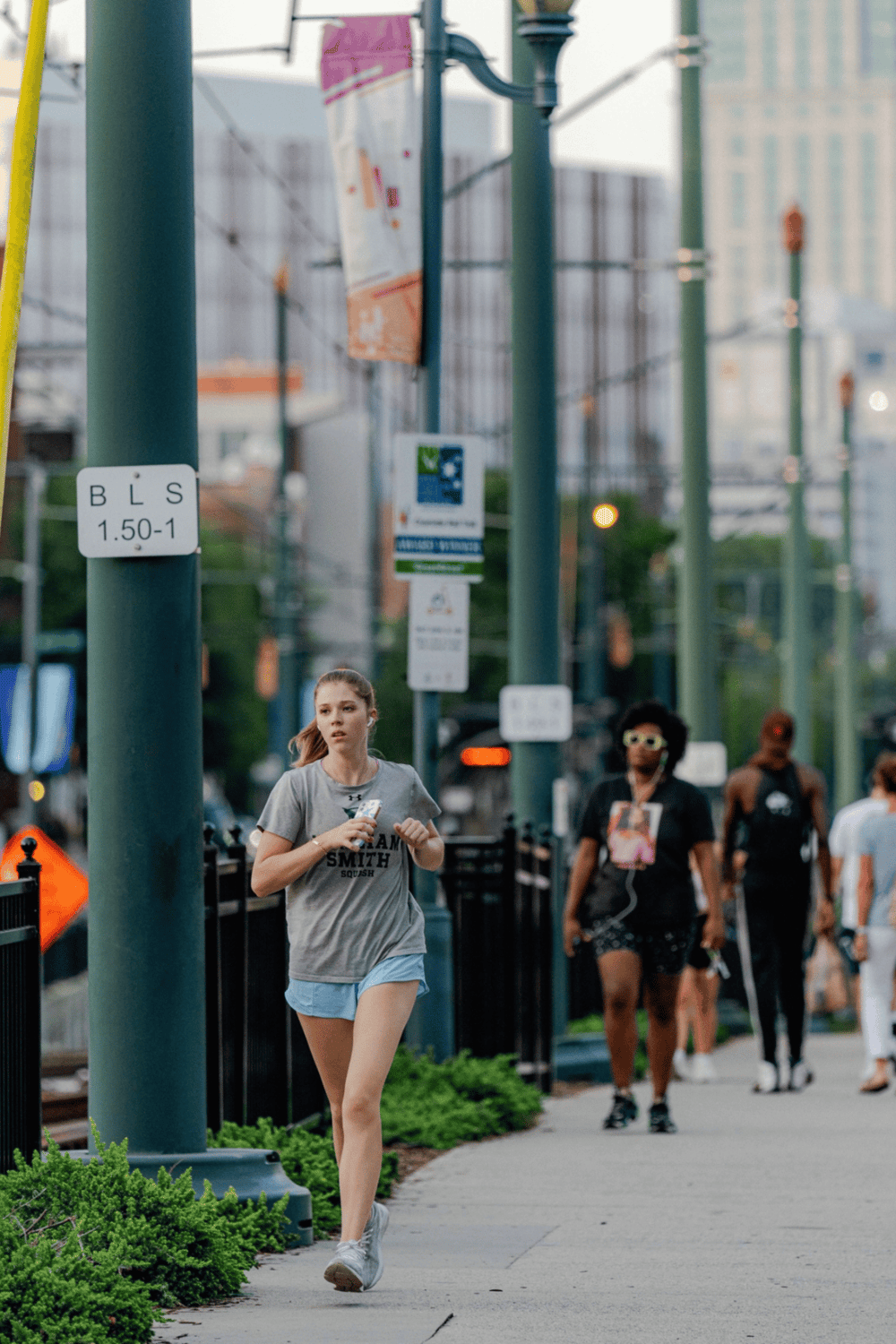 1. Young woman running on city sidewalk with transit signs and busy street background.