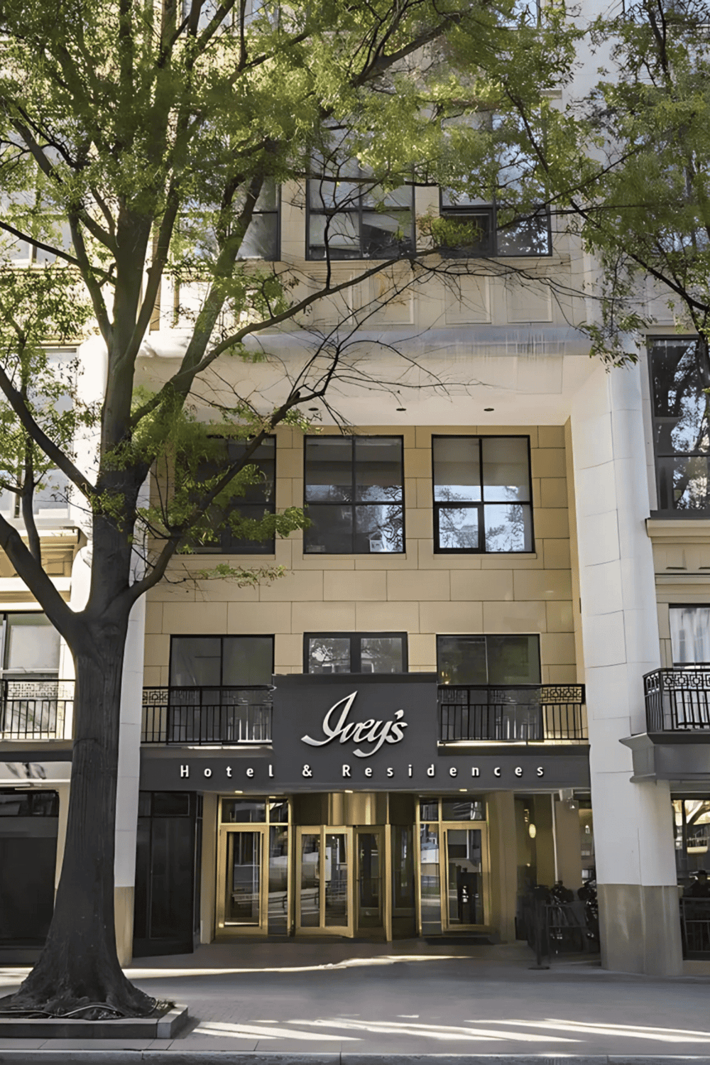 Modern hotel building with black and gold accents, surrounded by lush greenery in an urban setting.
