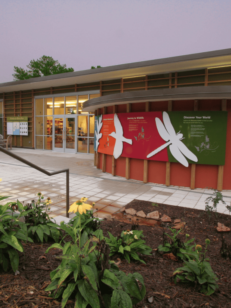 Brightly lit visitor center with nature-themed signage and flower beds outside, inviting exploration of wildlife and conservation.