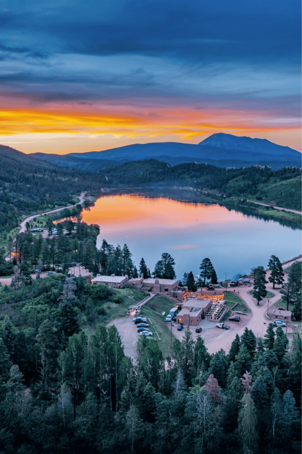 Serene mountain lake at sunset with surrounding trees and residential area, perfect for outdoor adventures.