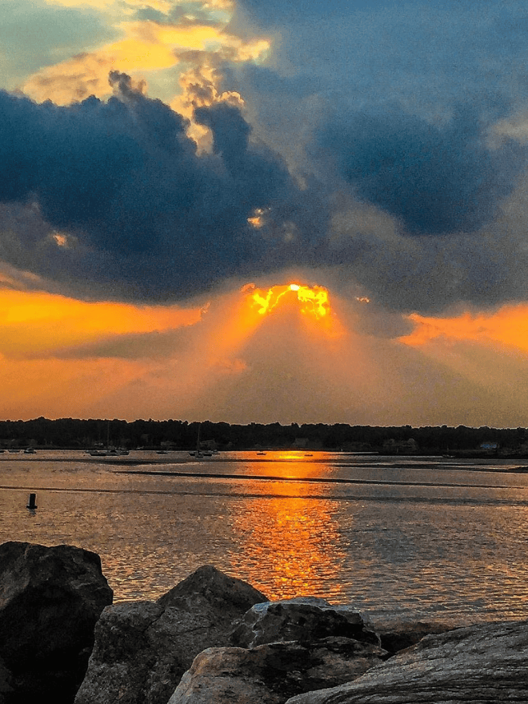 Golden sunset over water with rocks in foreground, peaceful scenic view.