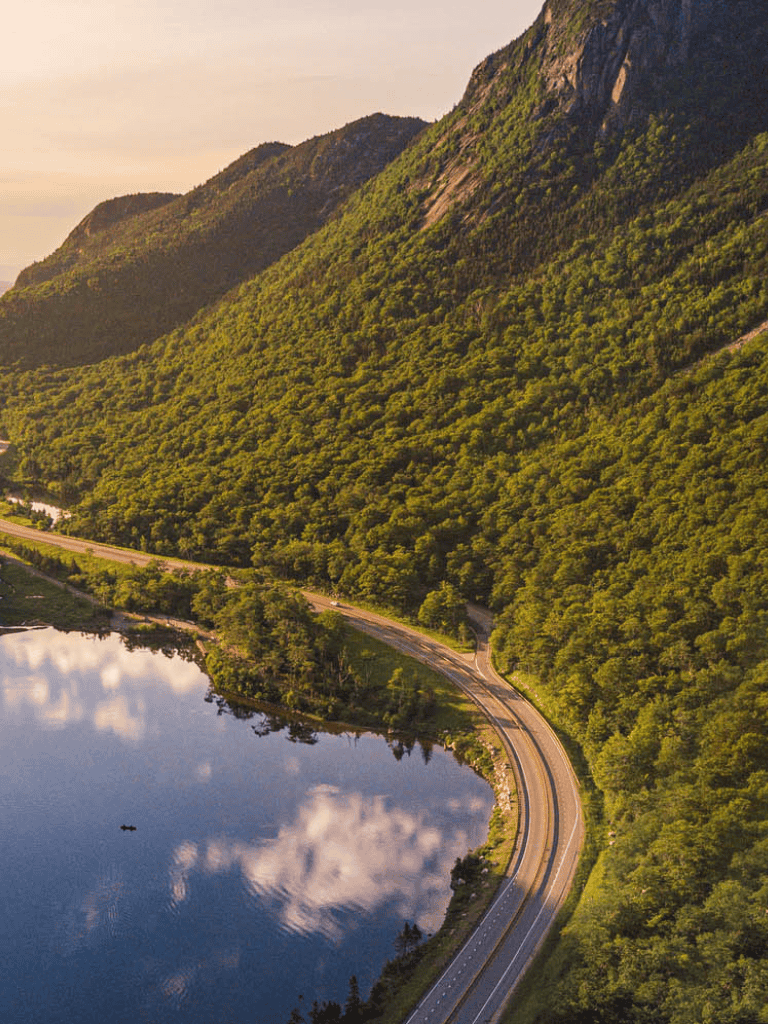 Serene mountain landscape with winding road and tranquil lake at sunset.