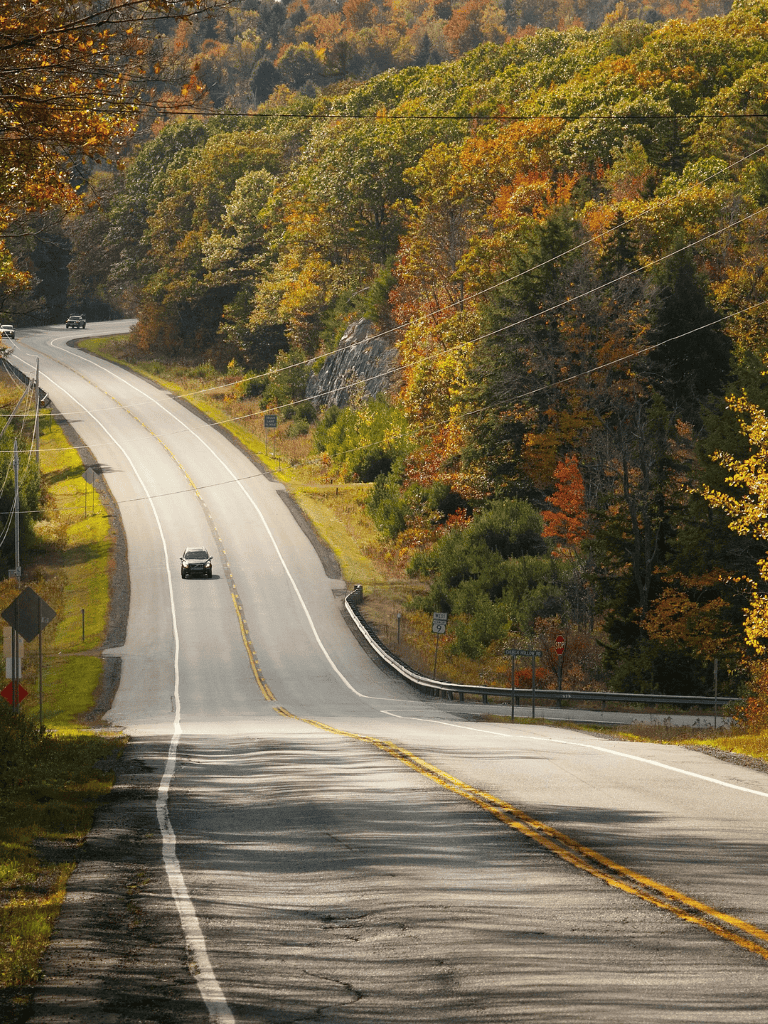 Winding rural highway surrounded by colorful fall foliage in the mountains.