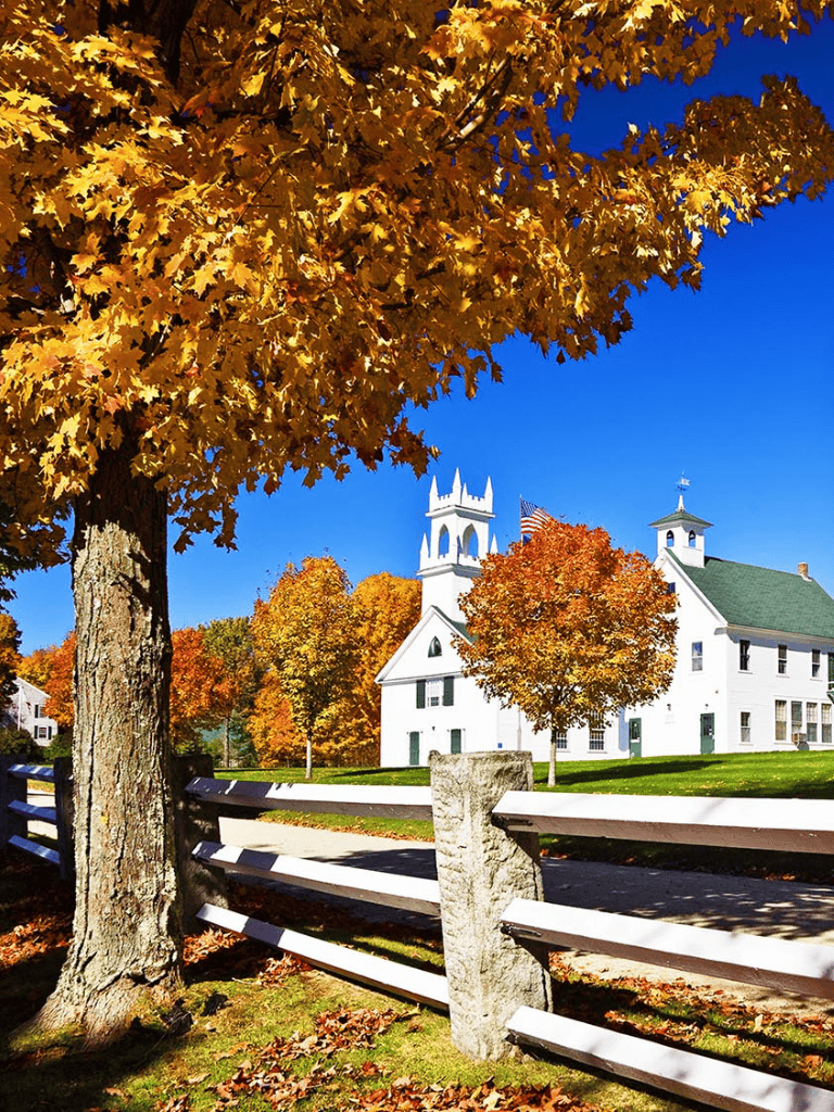 Vibrant fall foliage surrounding a white historic church under a clear blue sky.