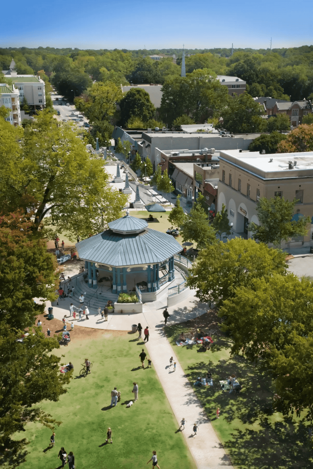 Aerial view of a vibrant downtown area with a park, bandstand, and surrounding commercial buildings, showcasing community and city life.