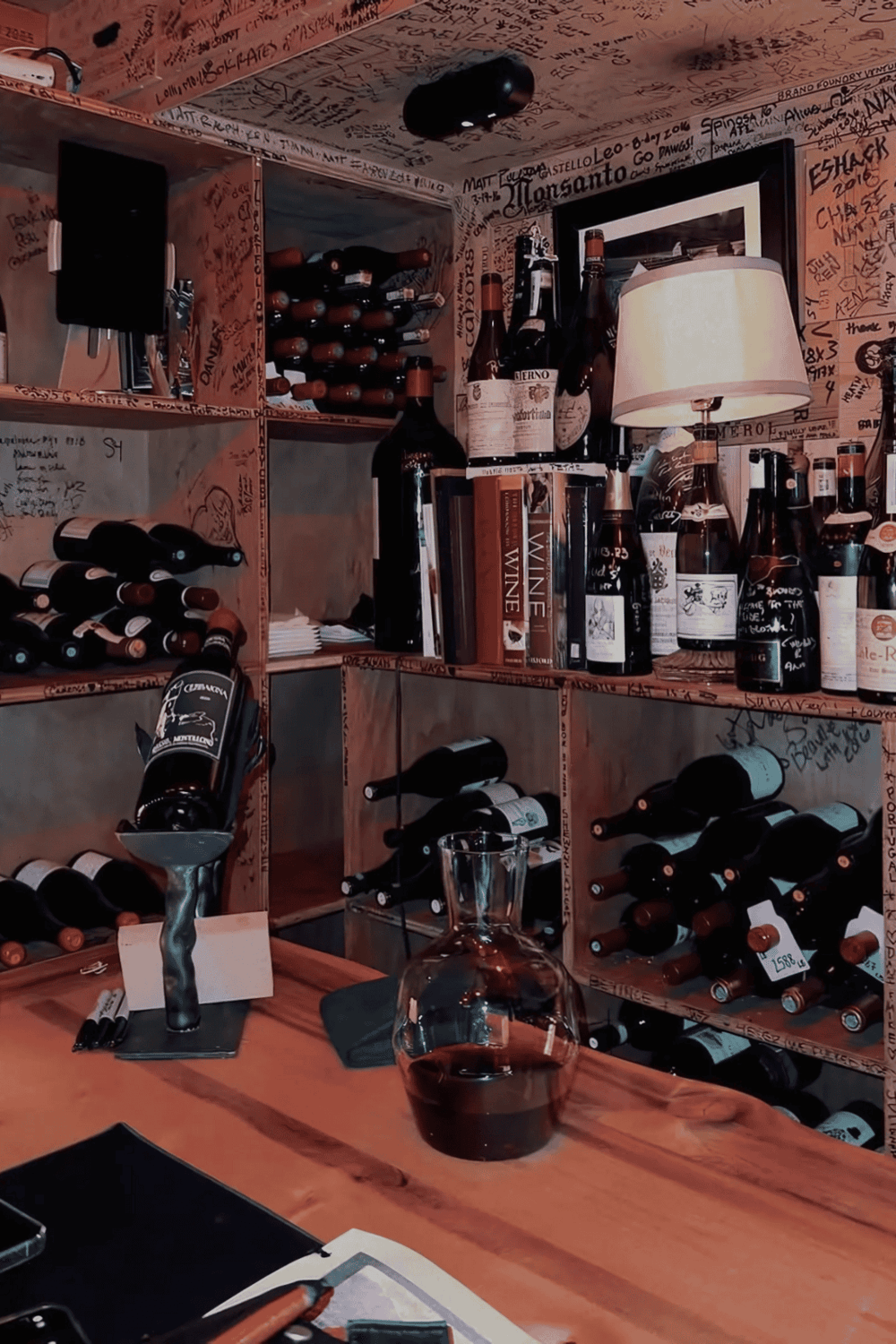 A cozy wine cellar with shelves filled with wine bottles, a glass of red wine on a wooden table, and warm ambient lighting.