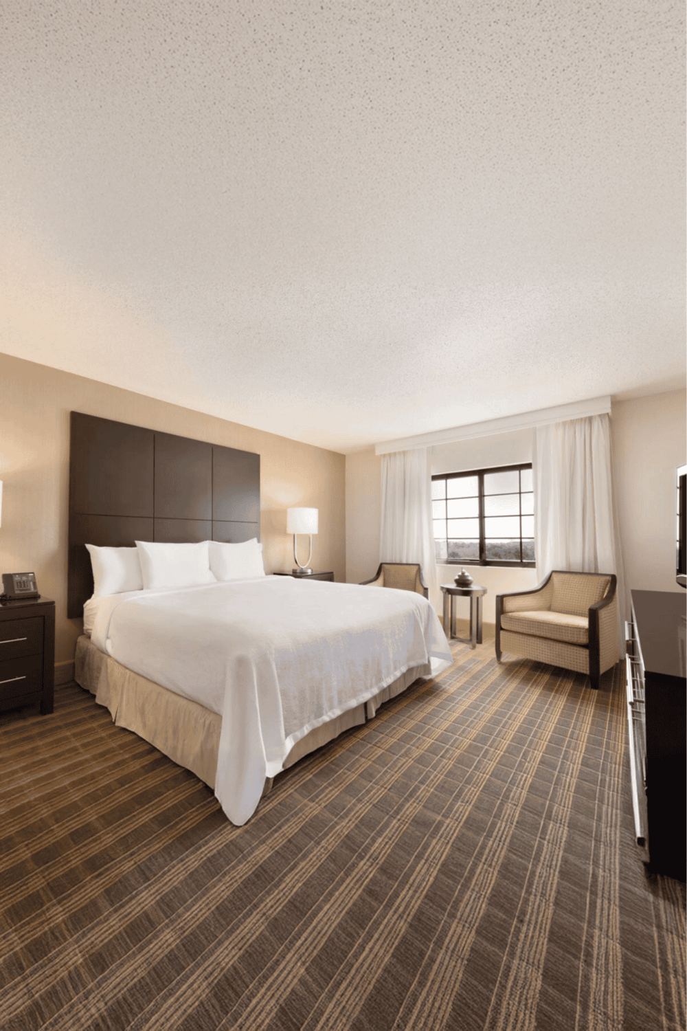 Spacious hotel room with king bed, modern furnishings, and large window for a comfortable stay.