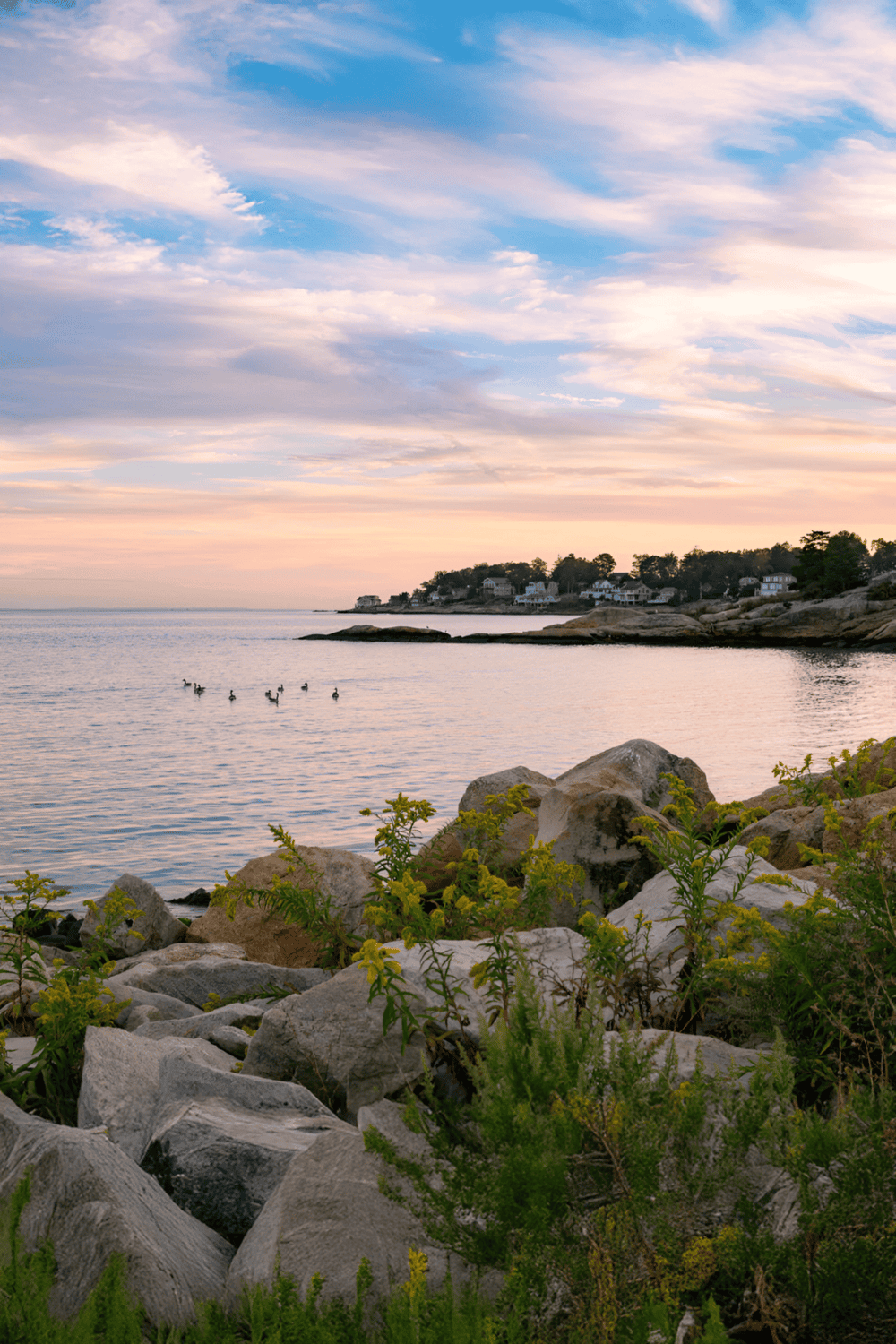 Tranquil coastal scene with rocks, water, and a colorful sky at sunset.