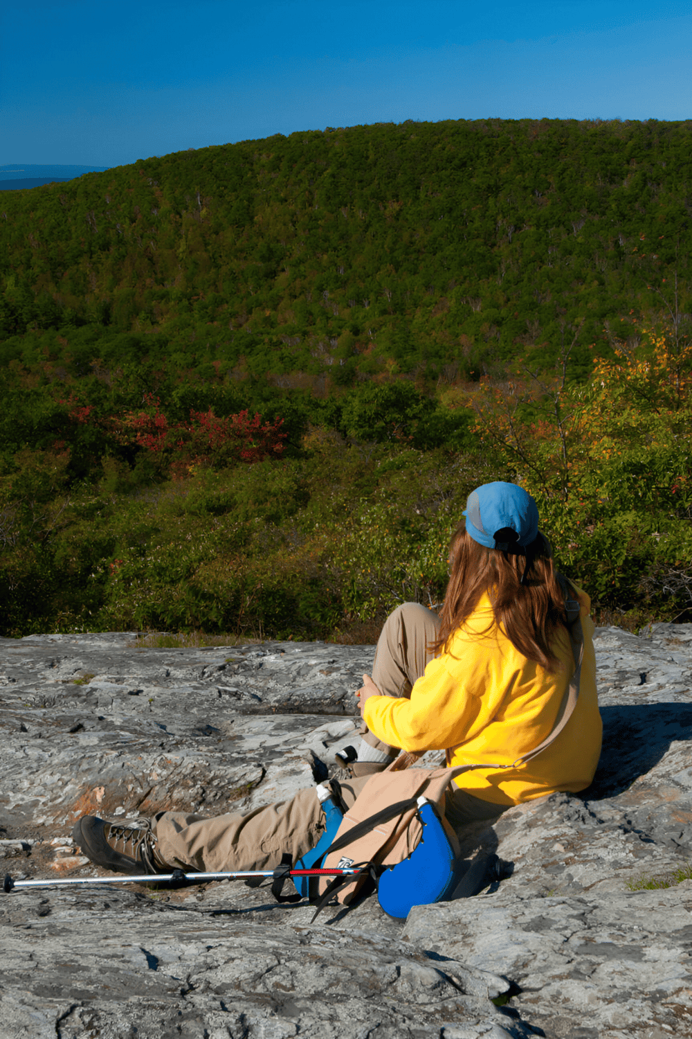 Hiker relaxing on rocky hilltop with scenic mountain view, outdoor adventure, trekking, and nature exploration.