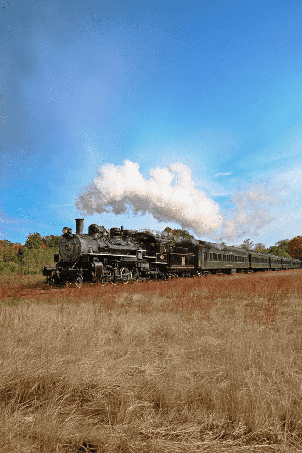 Steam train traveling through scenic fields with blue sky and autumn foliage, ideal for travel and adventure SEO keywords.
