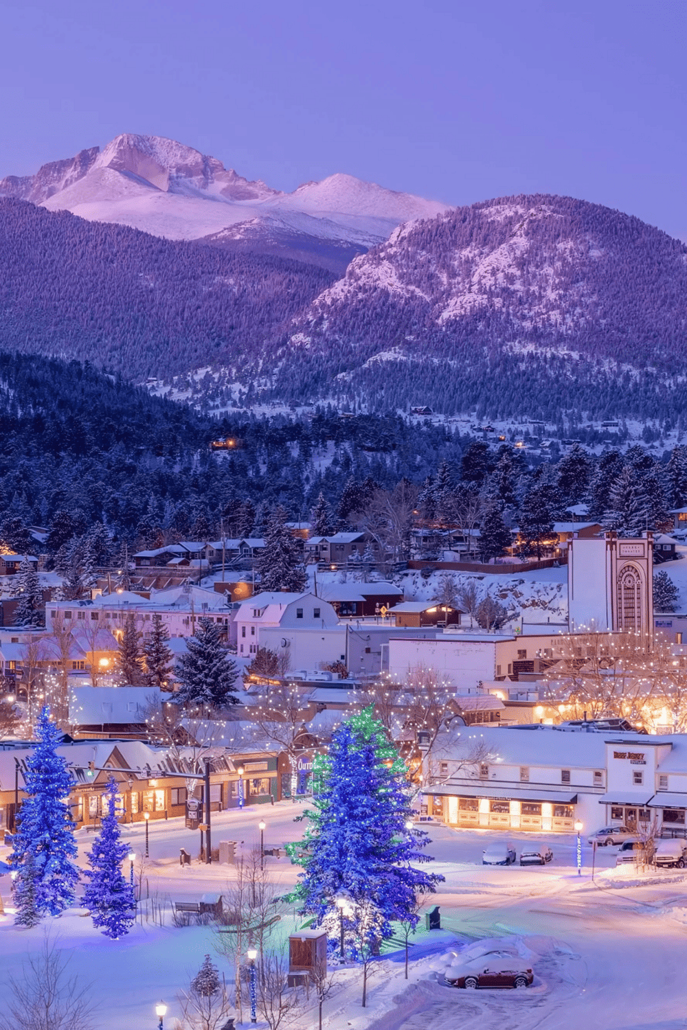 Snowy mountain town with festive holiday lights and decorated Christmas trees, winter scenery, mountain backdrop.