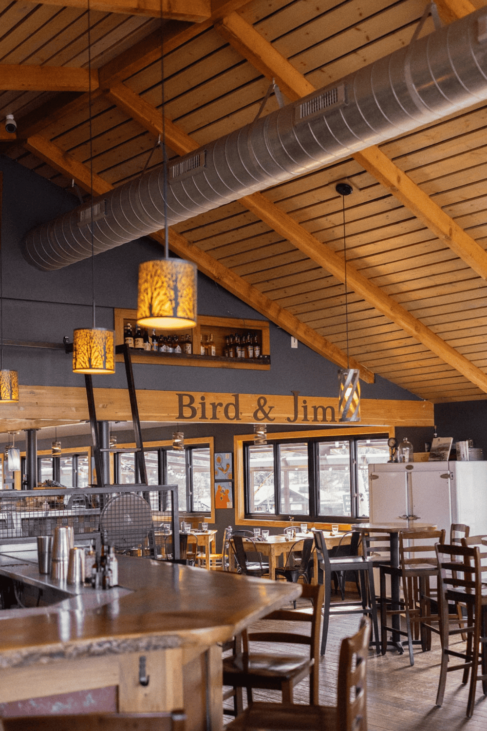 Cozy restaurant interior with wooden beams, pendant lighting, and a bar at Bird & Jim to enjoy great dining experiences.