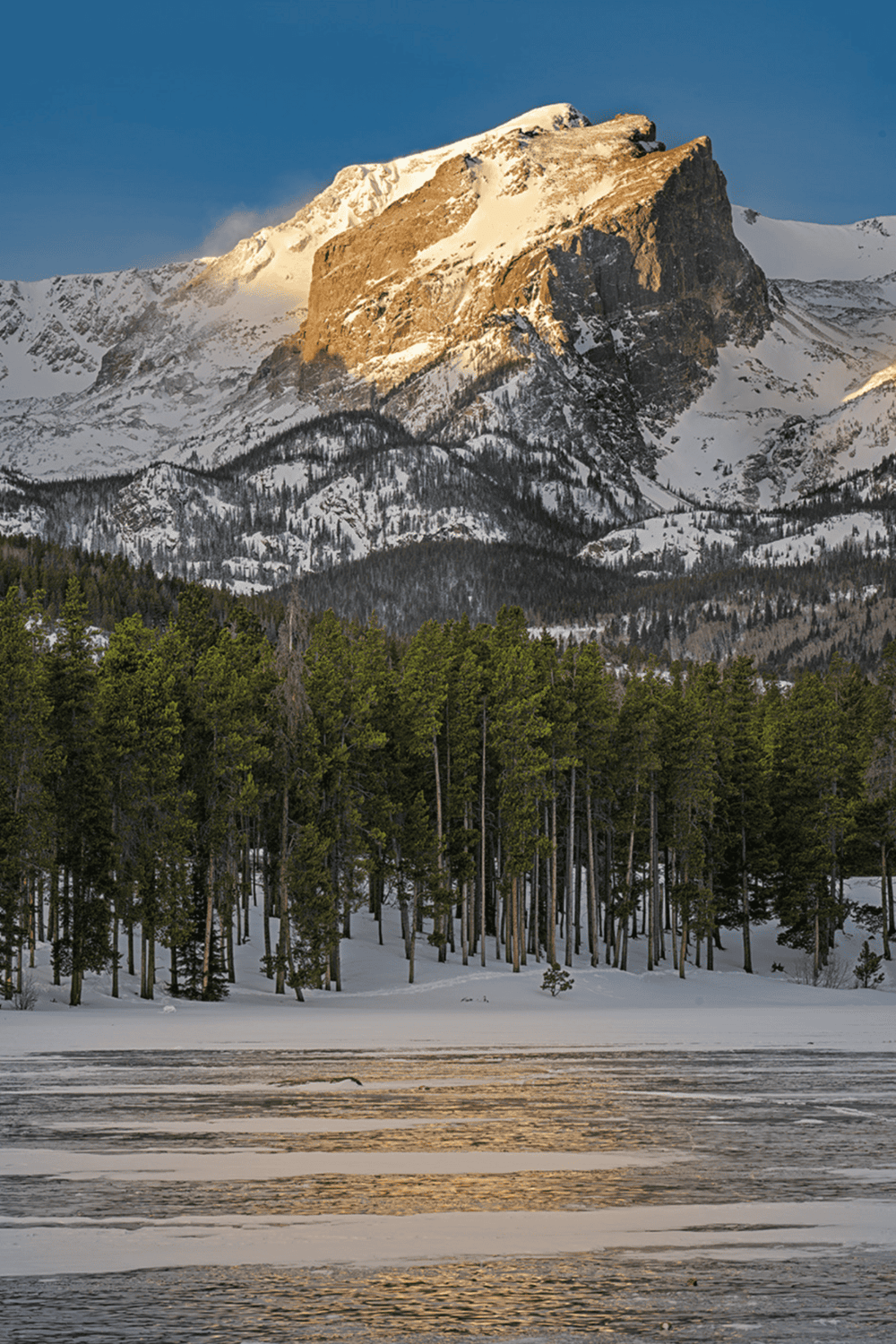 Snow-capped mountain with forest and frozen lake, scenic hiking destination, mountain adventure, nature exploration in winter.