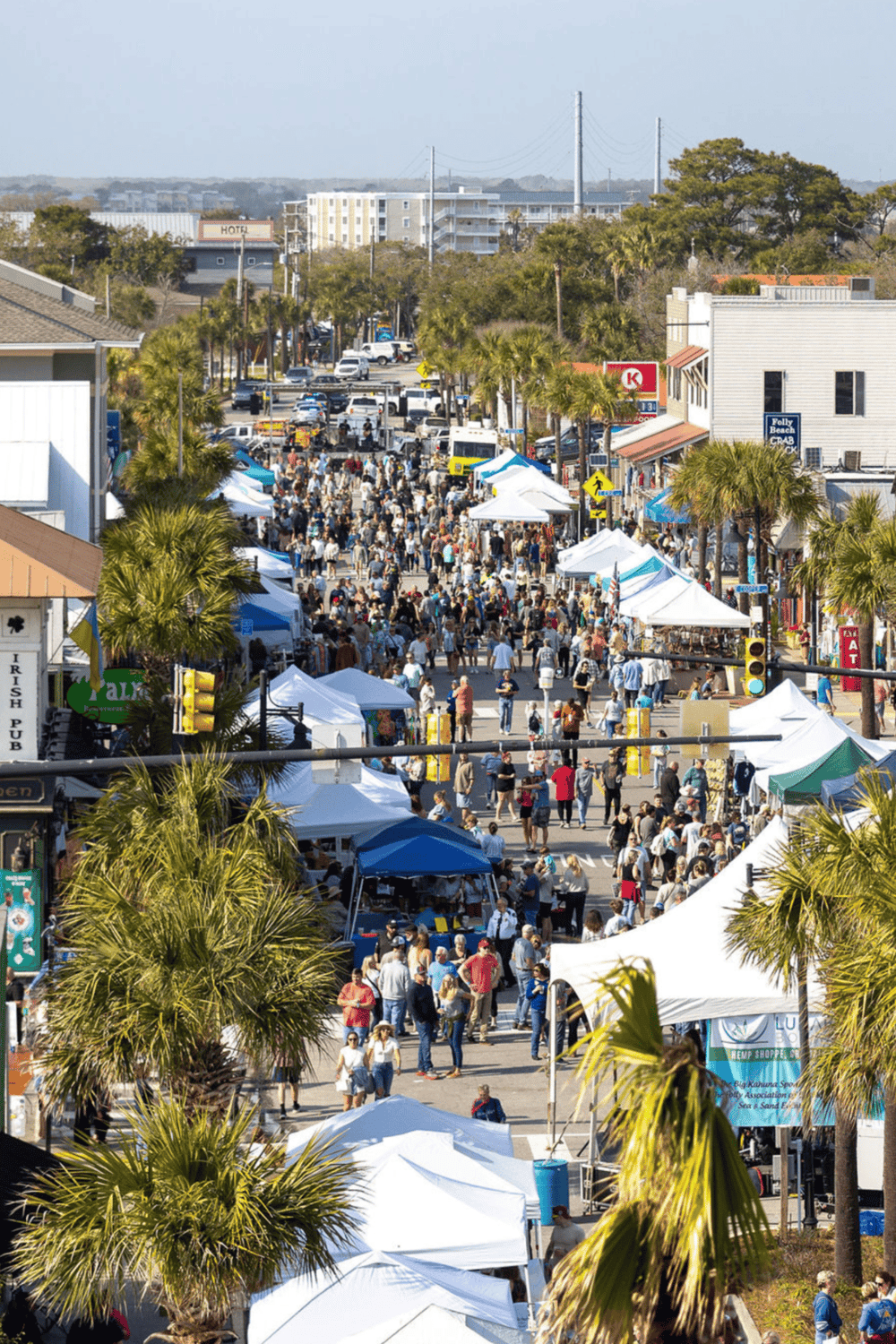 Crowded outdoor street market in Destin, Florida with tents, shoppers, palm trees, and businesses.