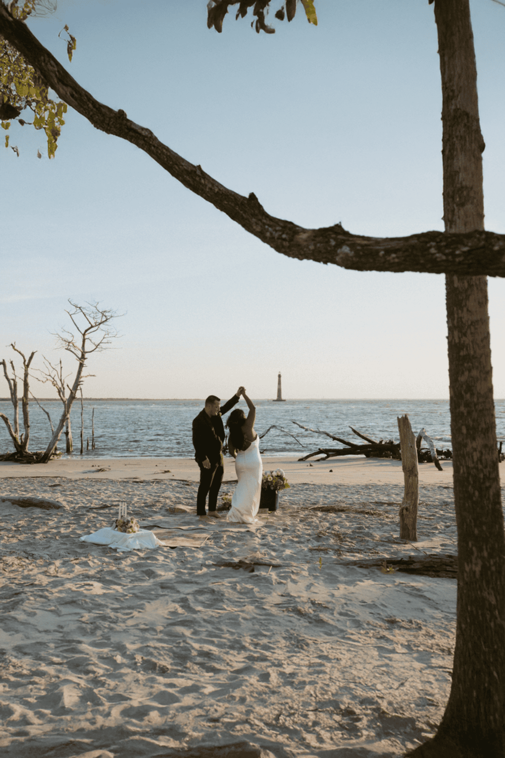 Romantic beach wedding ceremony at sunset, Gulf of Mexico, tall lighthouse in background.