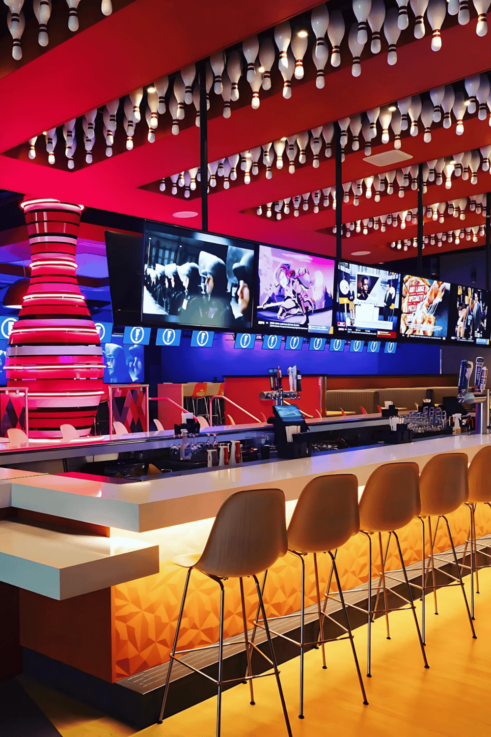 Bright modern sports bar with multiple TV screens, vibrant red and orange decor, and a sleek bar counter perfect for entertainment.