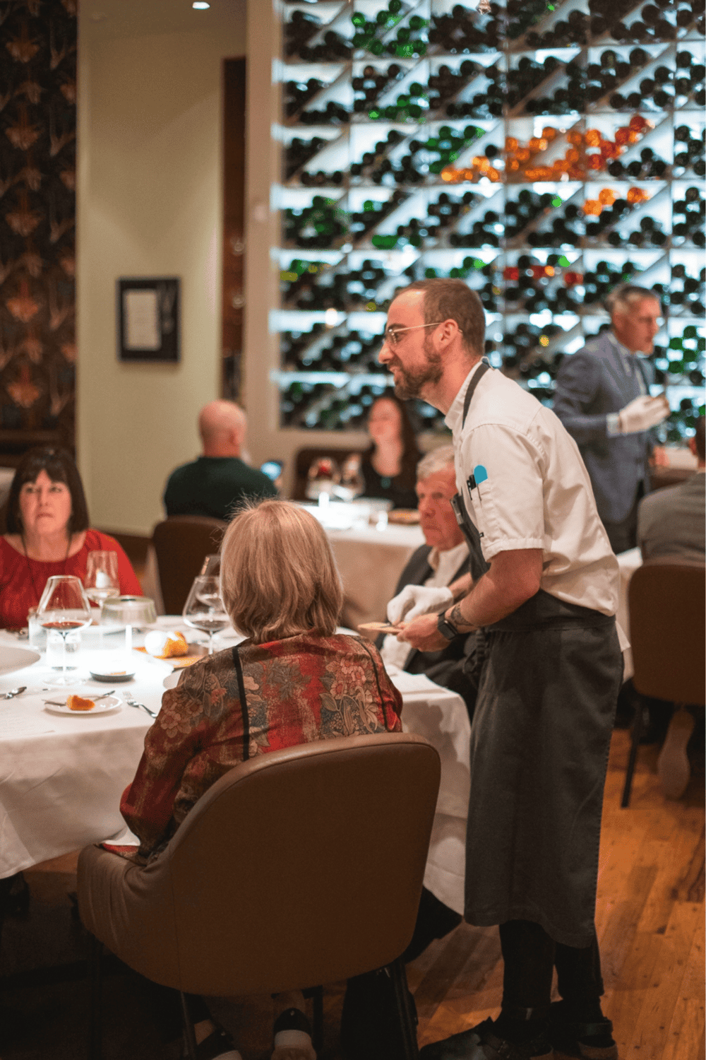 Elegant restaurant with wine wall and attentive staff serving guests.