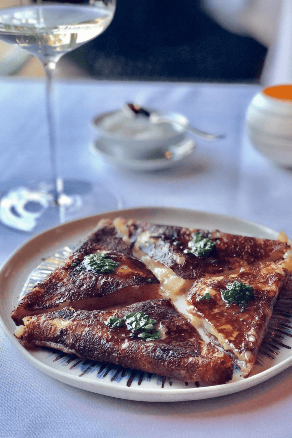 Thin crust pizza with herbs on a white plate in a restaurant setting.