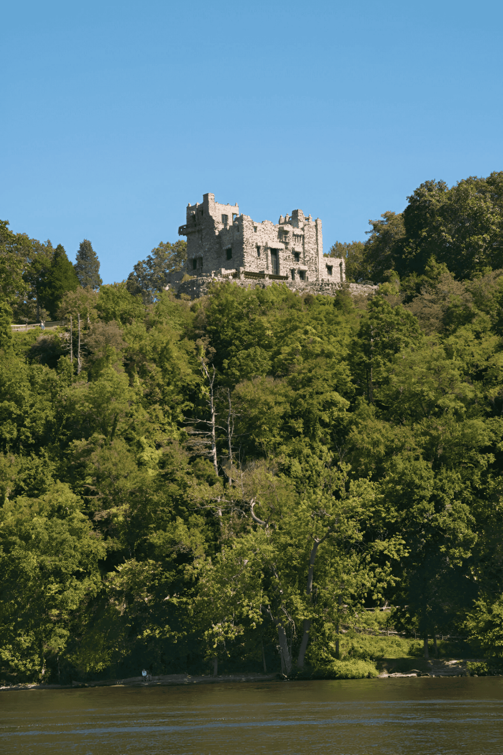 Ancient castle on lush green hilltop overlooking water, scenic historical site, popular tourism destination.