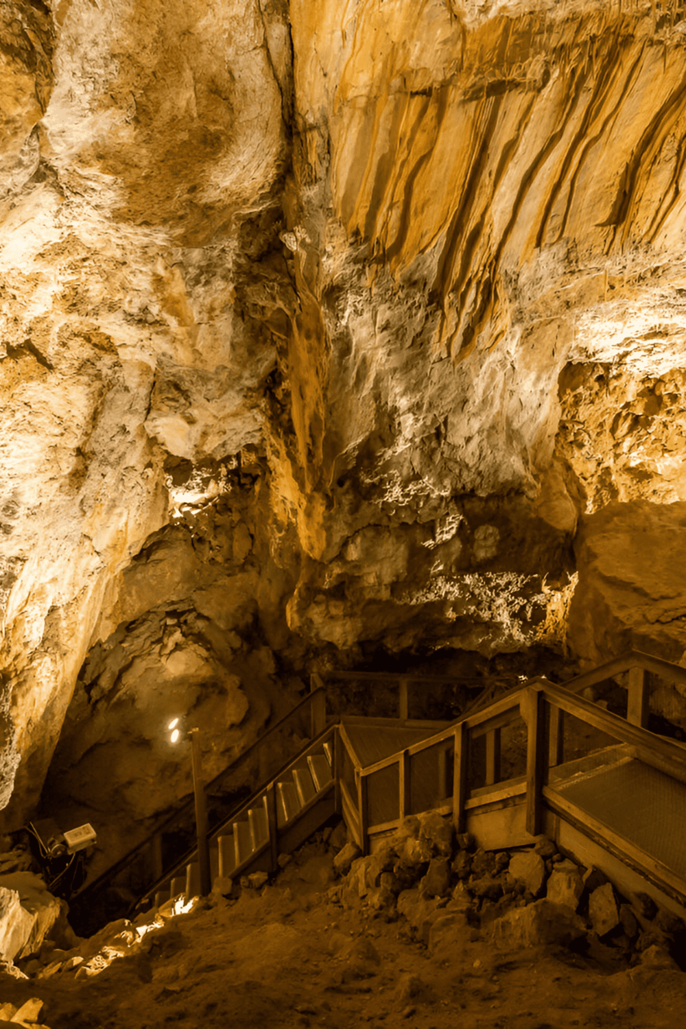 Stalactites and stalagmites in limestone cave with wooden stairs for visitors.